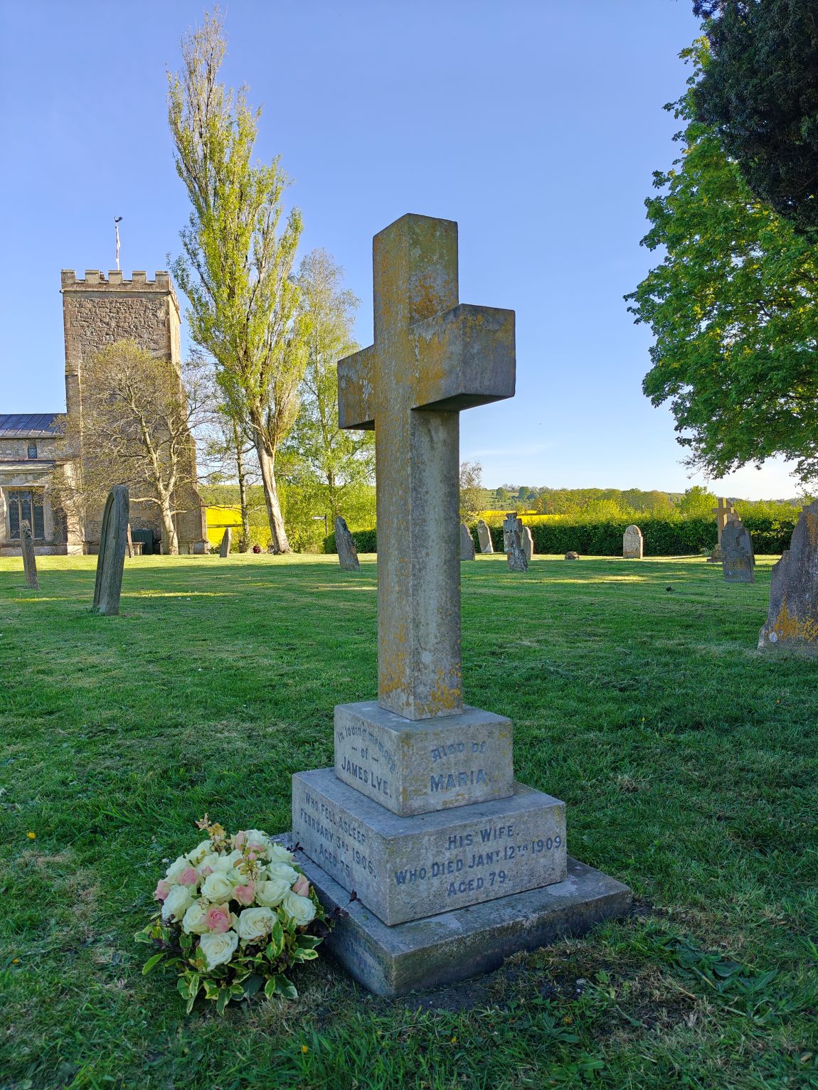 Image of James Lye's grave in the churchyard at Market Lavington Church, with a view towards the Church